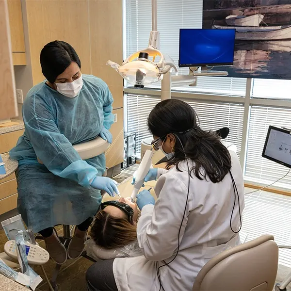 A dentist and an assistant examining a patient in a sunlit treatment room.